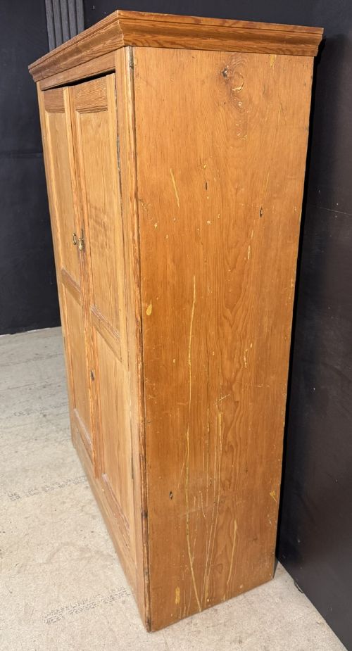 A freestanding double-door antique pine larder cupboard with four raised door panels, brass drop handles, a keyhole, and a moulded top cornice. View III