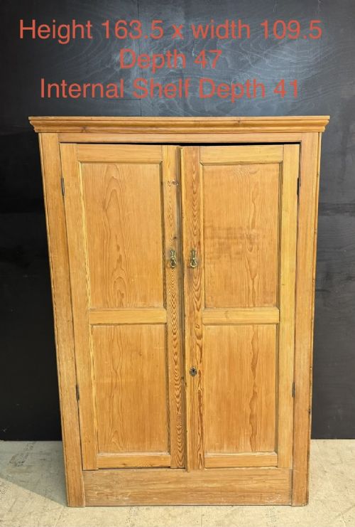 A freestanding double-door antique pine larder cupboard with four raised door panels, brass drop handles, a keyhole, and a moulded top cornice. View VI