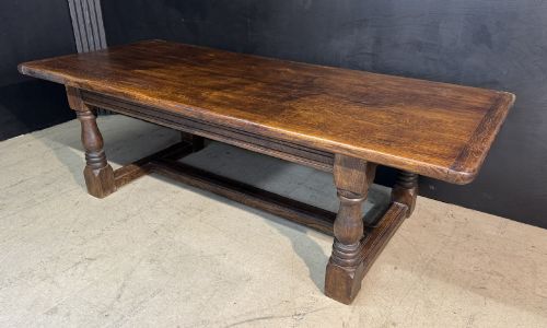 fig 1. A long and deep solid dark oak farmhouse dining table featuring a plank top, moulded apron, and thick turned baluster legs joined by a floor-level stretcher.