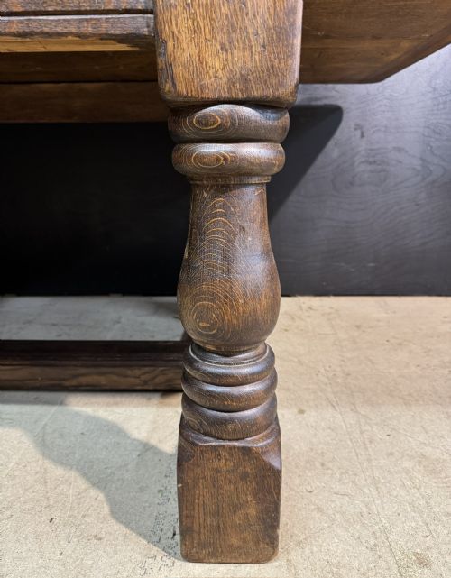 A long and deep solid dark oak farmhouse dining table featuring a plank top, moulded apron, and thick turned baluster legs joined by a floor-level stretcher. View XIV