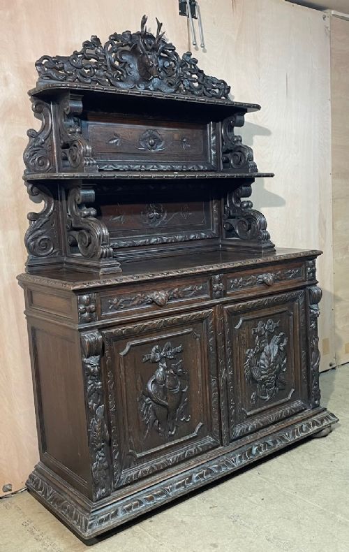 A dark oak French hunting sideboard featuring a carved stag head top pediment, open middle shelves, and lower cabinet doors decorated with carved game birds. View VI