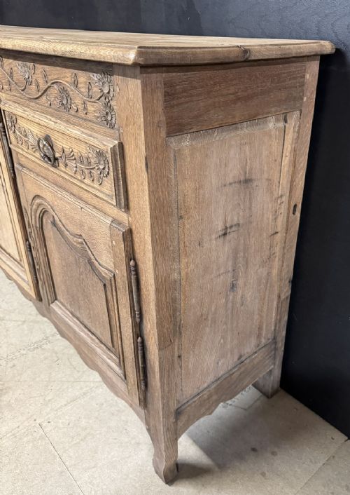 A long French oak enfilade featuring four cupboards with arched fielded panels, decorative floral carvings along the frieze, and two side drawers. View XI