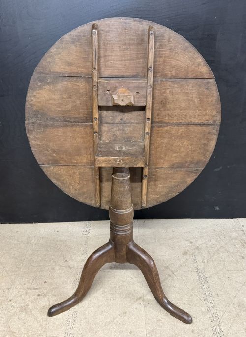 A circular Georgian oak tilt-top table positioned upright on a central turned column with three curved tripod legs. View III