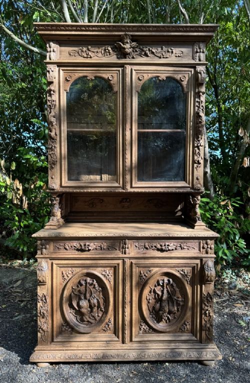 A two-piece bleached oak hunting cabinet featuring hand-carved relief panels of game birds, glazed upper doors, and a decorative mask pediment. View II