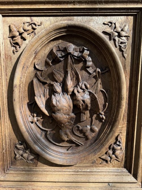 A two-piece bleached oak hunting cabinet featuring hand-carved relief panels of game birds, glazed upper doors, and a decorative mask pediment. View V