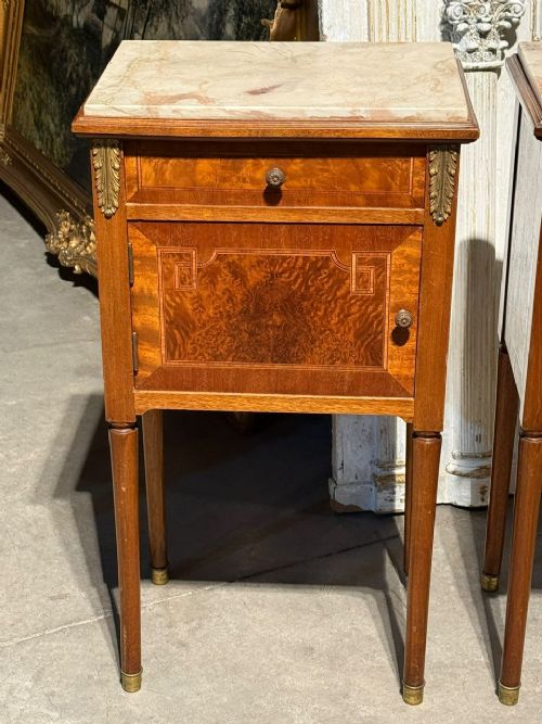 A pair of French Louis XVI style wooden bedside cabinets featuring marble tops, single drawers, inlaid cupboard doors, and gilt brass mounts on slender tapered legs. View VIII