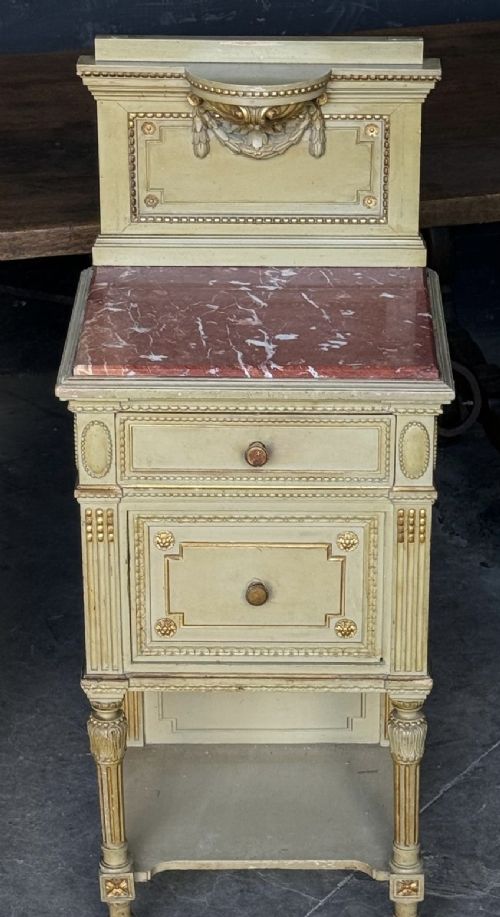 A matching pair of painted French neoclassical bedside cabinets featuring red marble tops, carved bracket superstructures, gold leaf detailing, drawers, and open lower shelves. View V