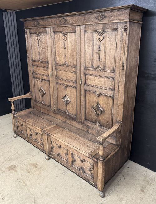 A large carved oak hall bench featuring a high back with three cupboard doors, geometric diamond panelling, and a lift-top storage seat. View IV