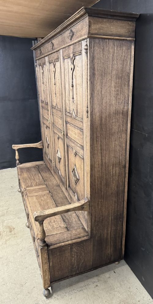 A large carved oak hall bench featuring a high back with three cupboard doors, geometric diamond panelling, and a lift-top storage seat. View XI