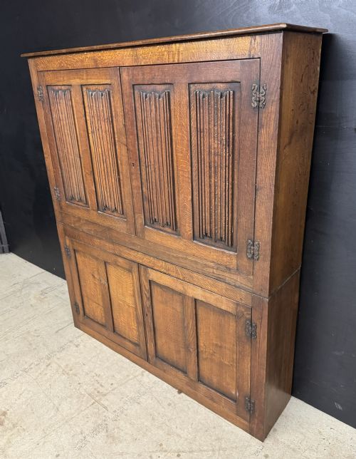 A narrow dark oak hall cupboard featuring upper carved linenfold doors and lower plain panel doors with iron hinges. View IV