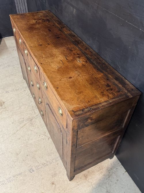 A Georgian Welsh oak dresser base with multiple drawers and two panelled cupboard doors featuring brass drop handles. View XI