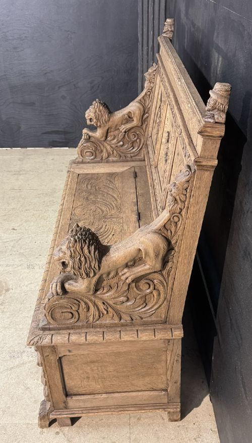 A French carved oak hall bench featuring relief panels depicting tavern scenes, lion figure armrests, and mask carvings on the base. View XI