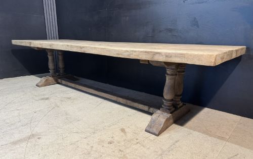 fig 1. An extra long natural oak refectory dining table featuring a timber plank top supported by twin turned baluster trestle legs connected by a floor-level stretcher.
