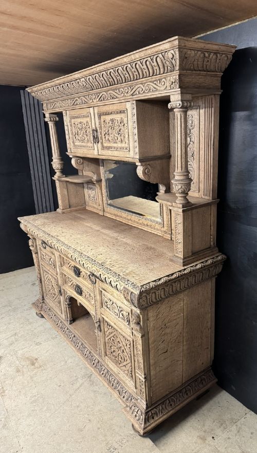 A large carved light oak sideboard with an upper cupboard section, a central mirror plate, turned columns, and detailed relief carvings throughout. View X