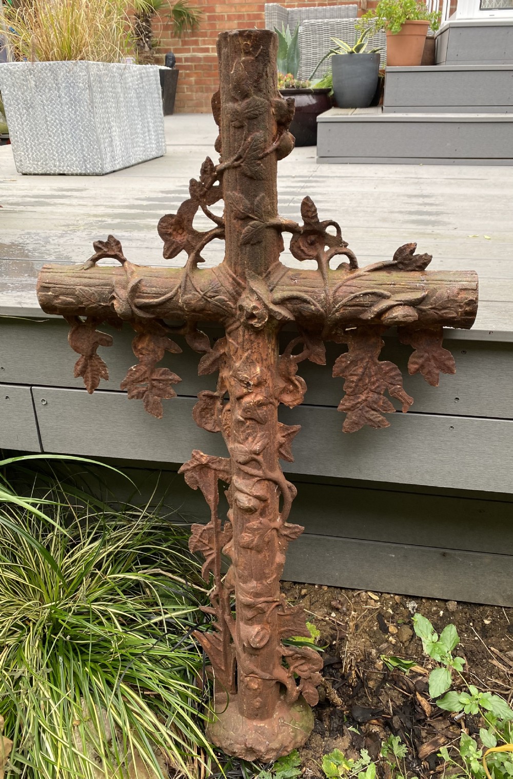A heavy cast iron cross featuring a faux-bois log texture wrapped in detailed trailing ivy leaves with a oxidized brown surface.