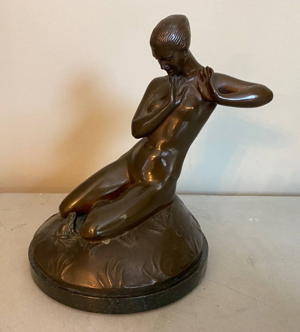 An Art Deco dark patinated bronze sculpture depicting a kneeling nude woman interacting with a small frog, mounted on a circular black marble base.