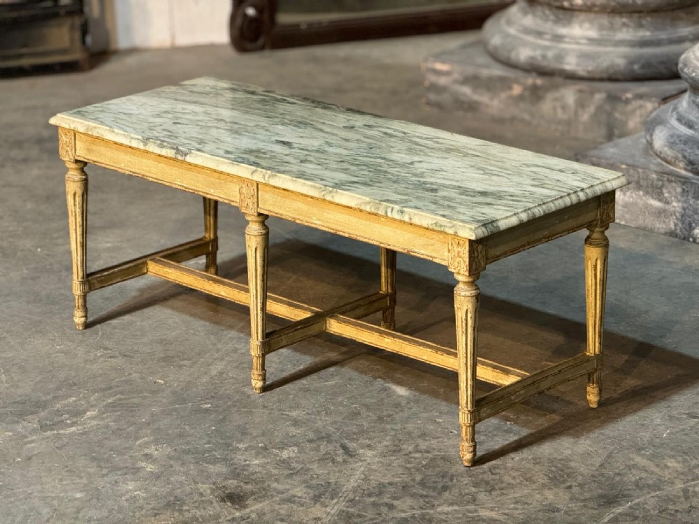 A low rectangular coffee table featuring a light green veined marble top set upon a distressed cream painted frame with six fluted legs and cross stretchers.