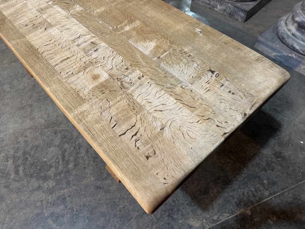 A rustic bleached oak dining table featuring a thick rectangular top supported by carved trestle ends connected with a stretcher beam. View XXIV