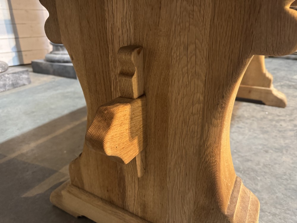 A rustic bleached oak dining table featuring a thick rectangular top supported by carved trestle ends connected with a stretcher beam. View XXVIII
