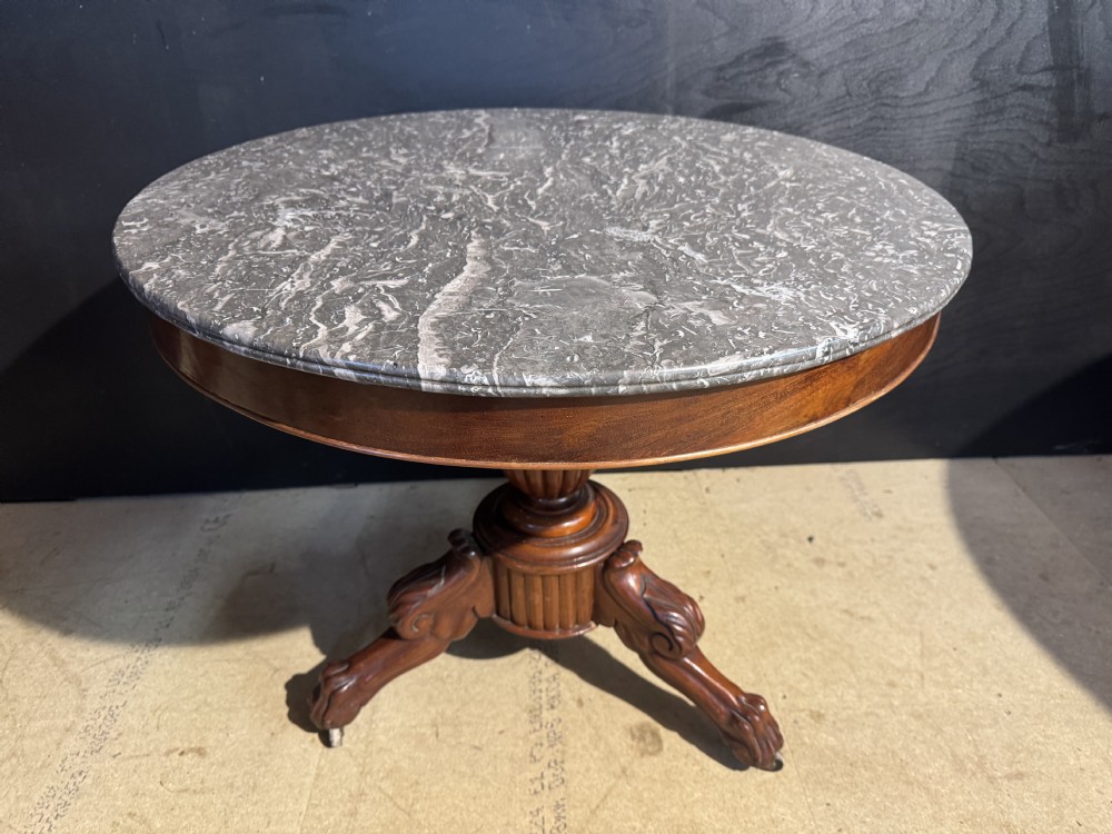 A circular 19th-century French gueridon table featuring a grey veined marble top resting on a carved mahogany fluted pedestal with tripod legs.