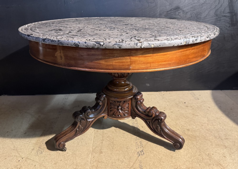 A circular 19th-century French centre table featuring a grey mottled marble top set on a carved wooden pedestal with tripod scroll feet.