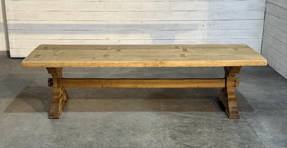 A large light oak farmhouse dining table featuring a solid plank top reinforced with butterfly joints and a sturdy trestle base connected by a central stretcher.
