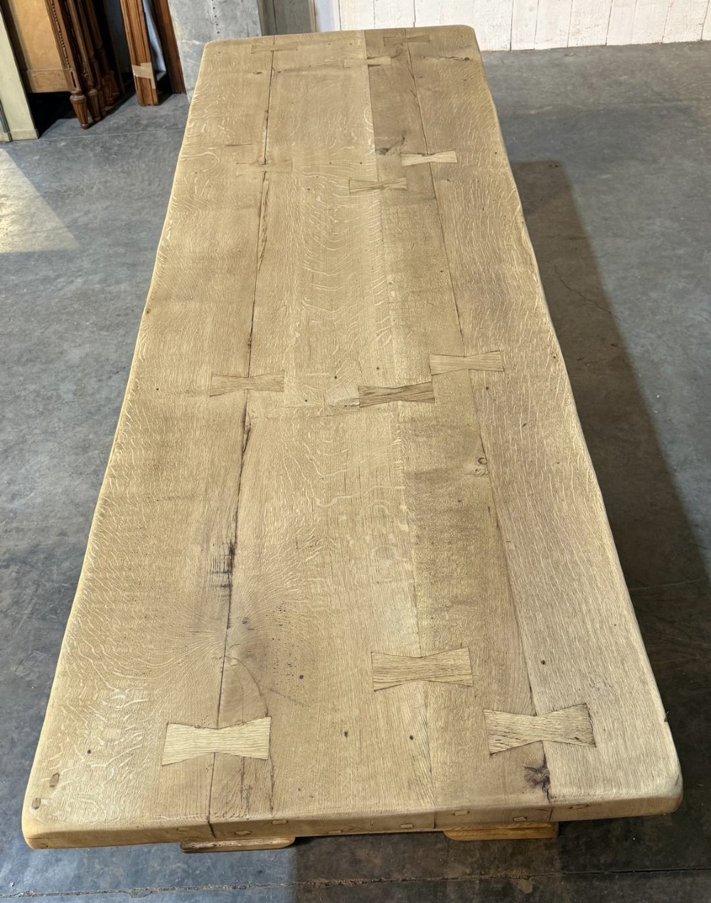 A large light oak farmhouse dining table featuring a solid plank top reinforced with butterfly joints and a sturdy trestle base connected by a central stretcher. View II