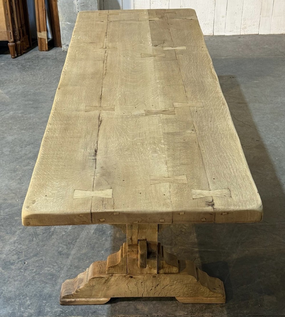 A large light oak farmhouse dining table featuring a solid plank top reinforced with butterfly joints and a sturdy trestle base connected by a central stretcher. View V