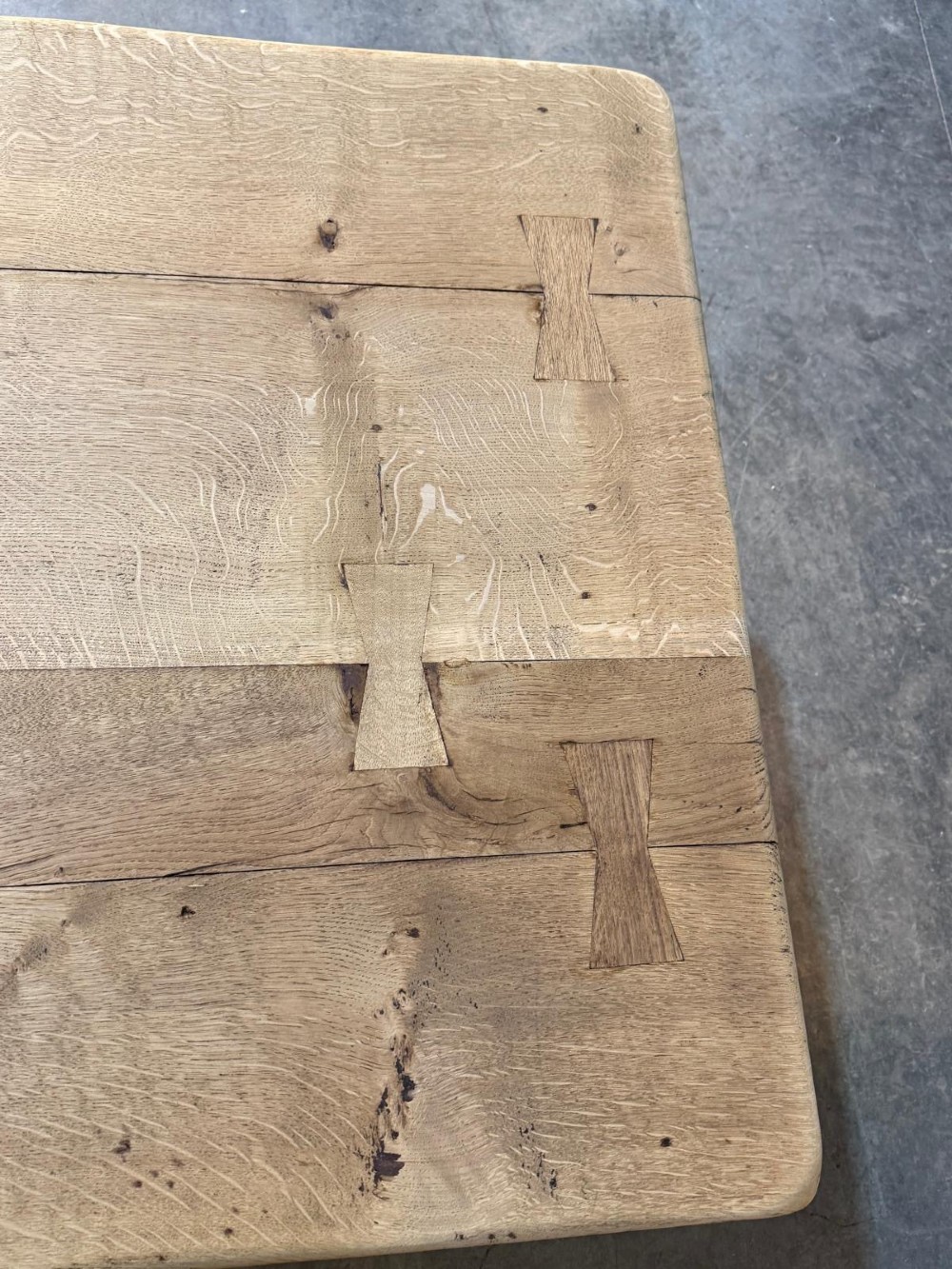 A large light oak farmhouse dining table featuring a solid plank top reinforced with butterfly joints and a sturdy trestle base connected by a central stretcher. View VIII