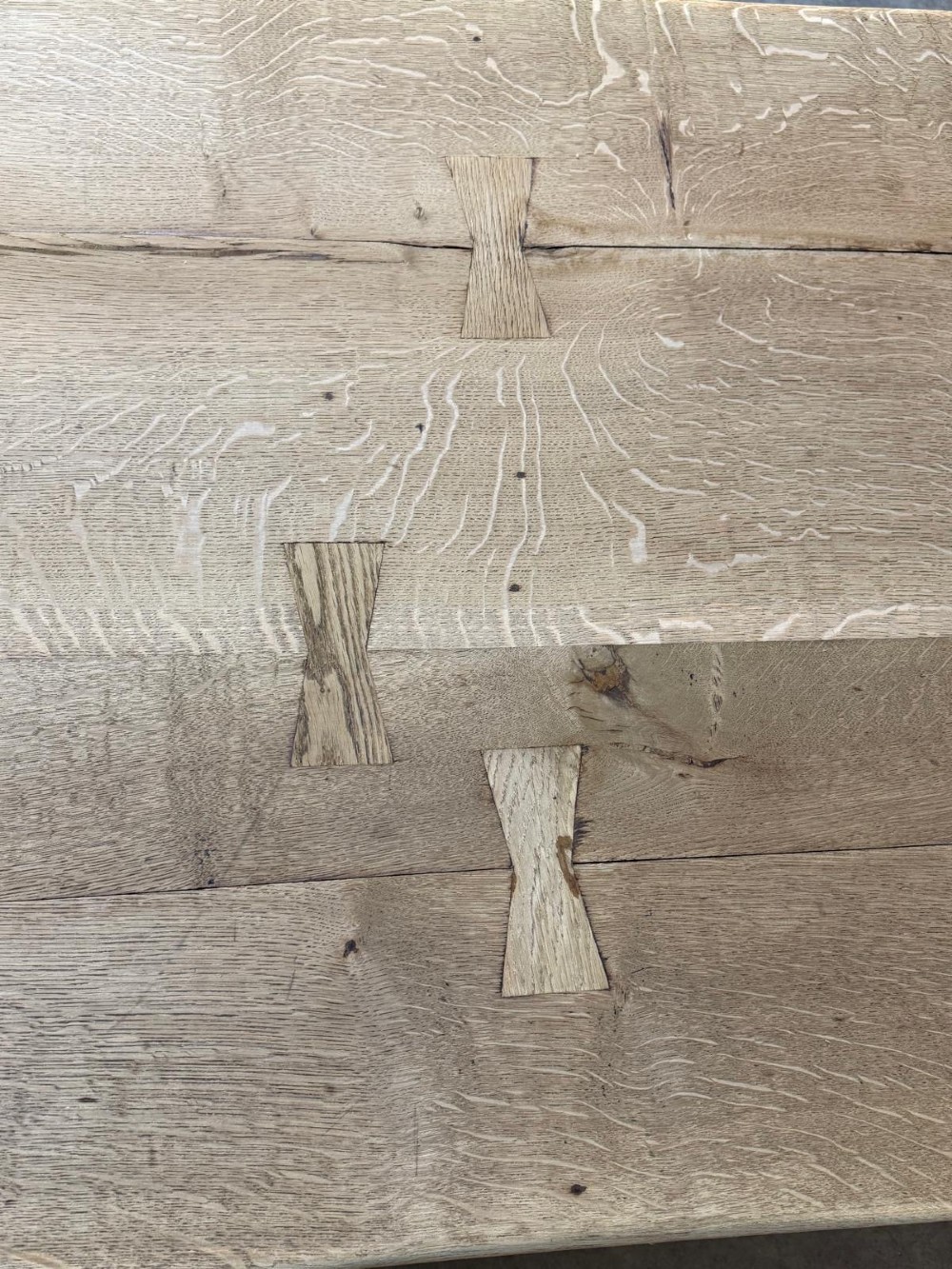 A large light oak farmhouse dining table featuring a solid plank top reinforced with butterfly joints and a sturdy trestle base connected by a central stretcher. View IX