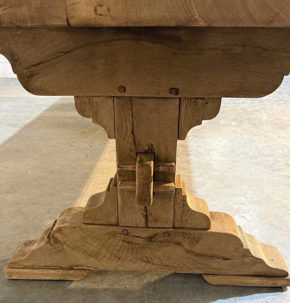 A large light oak farmhouse dining table featuring a solid plank top reinforced with butterfly joints and a sturdy trestle base connected by a central stretcher. View XI