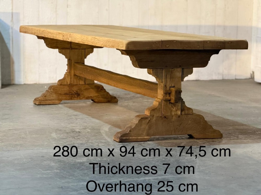 A large light oak farmhouse dining table featuring a solid plank top reinforced with butterfly joints and a sturdy trestle base connected by a central stretcher. View XII