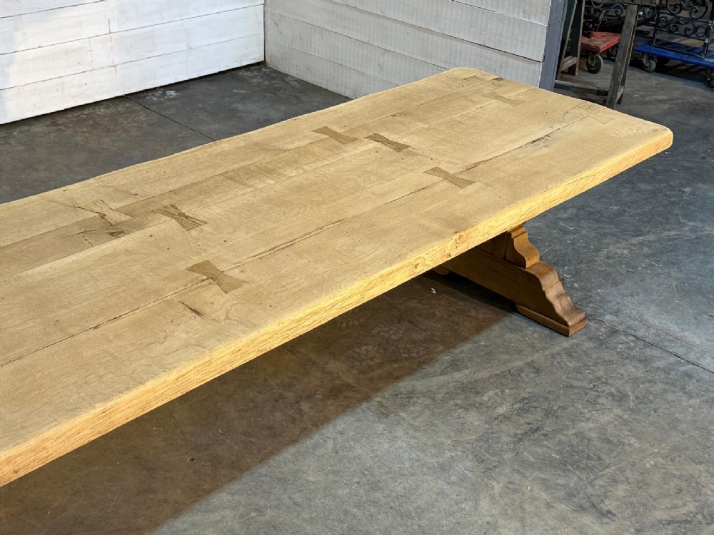 A large light oak farmhouse dining table featuring a solid plank top reinforced with butterfly joints and a sturdy trestle base connected by a central stretcher. View XIII