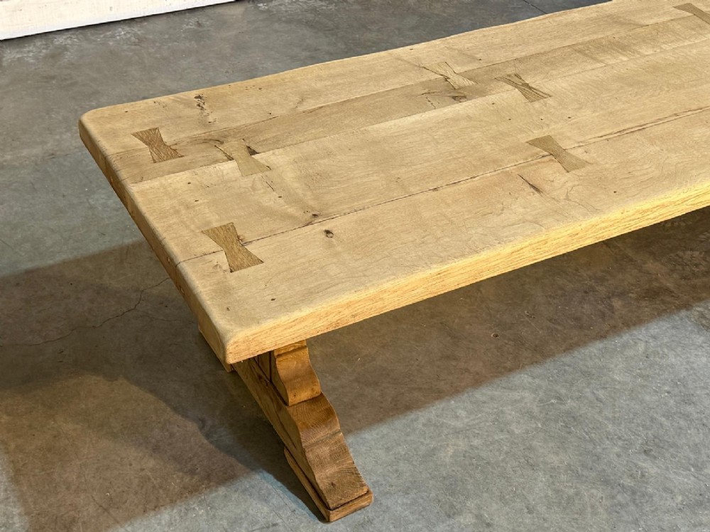 A large light oak farmhouse dining table featuring a solid plank top reinforced with butterfly joints and a sturdy trestle base connected by a central stretcher. View XIV