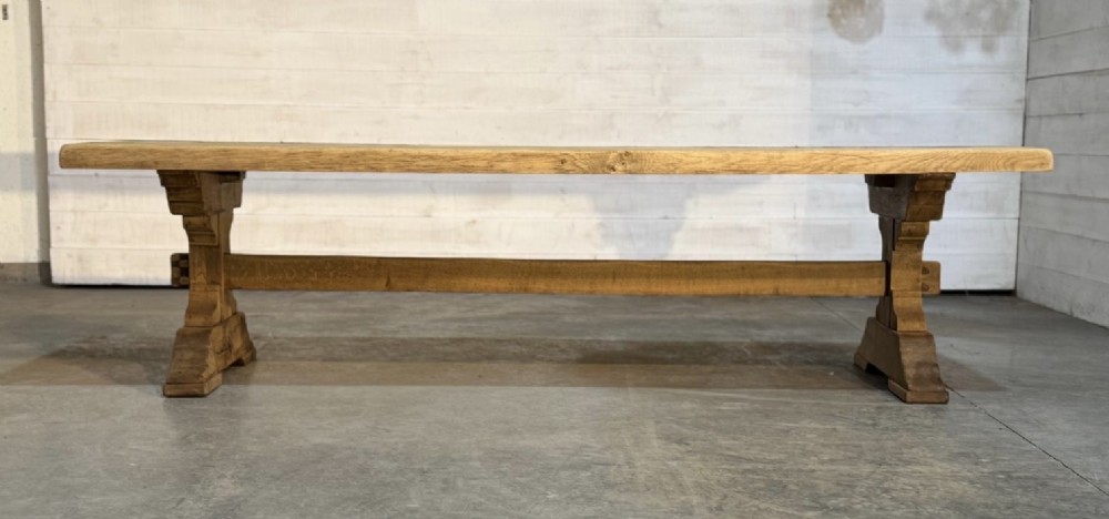 A large light oak farmhouse dining table featuring a solid plank top reinforced with butterfly joints and a sturdy trestle base connected by a central stretcher. View XV