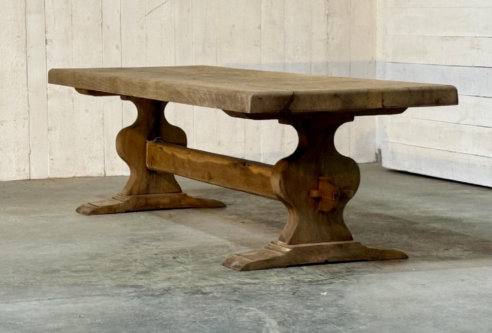 A large rustic French oak dining table featuring a thick timber plank top supported by a sturdy trestle base with a central keyed stretcher. View II