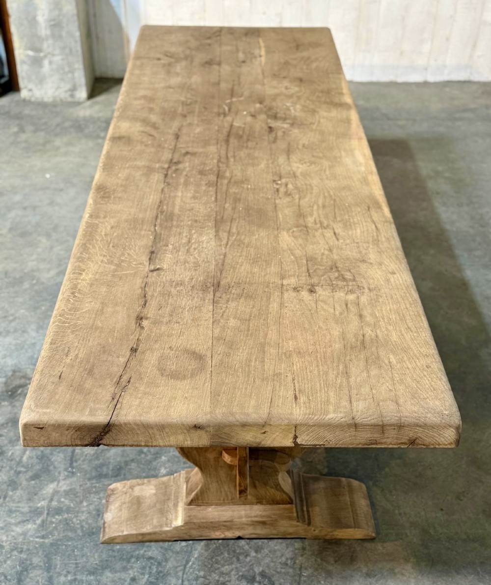 A large rustic French oak dining table featuring a thick timber plank top supported by a sturdy trestle base with a central keyed stretcher. View III