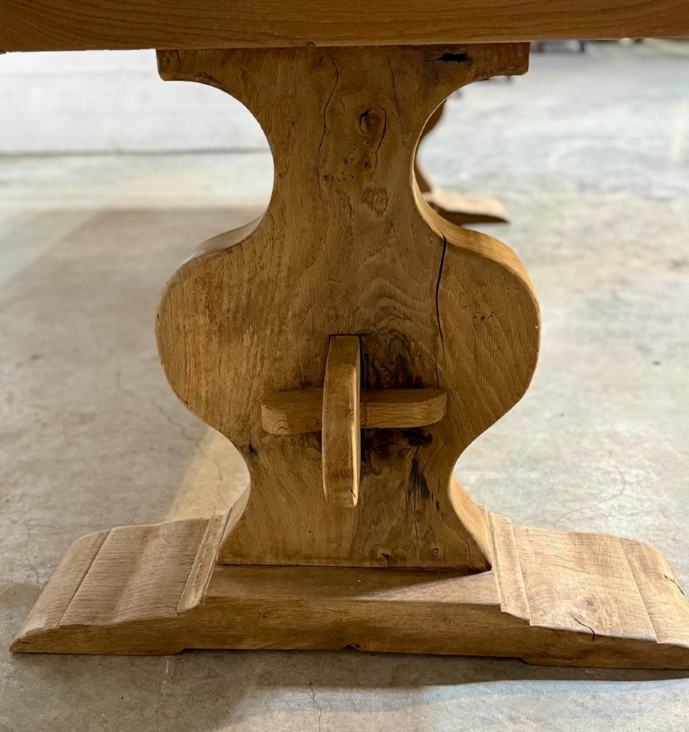 A large rustic French oak dining table featuring a thick timber plank top supported by a sturdy trestle base with a central keyed stretcher. View V