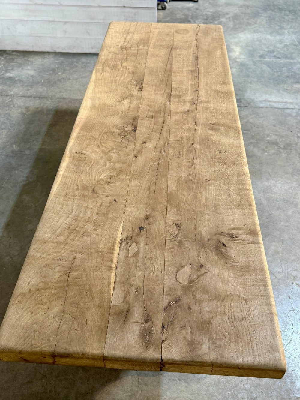 A large rustic French oak dining table featuring a thick timber plank top supported by a sturdy trestle base with a central keyed stretcher. View VI