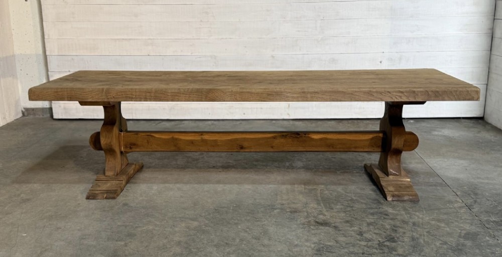 A large rustic French oak dining table featuring a thick timber plank top supported by a sturdy trestle base with a central keyed stretcher. View XI