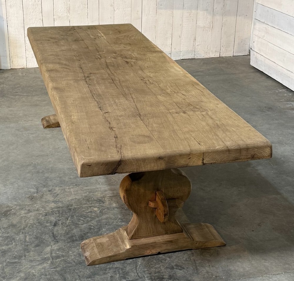 A large rustic French oak dining table featuring a thick timber plank top supported by a sturdy trestle base with a central keyed stretcher. View XIII