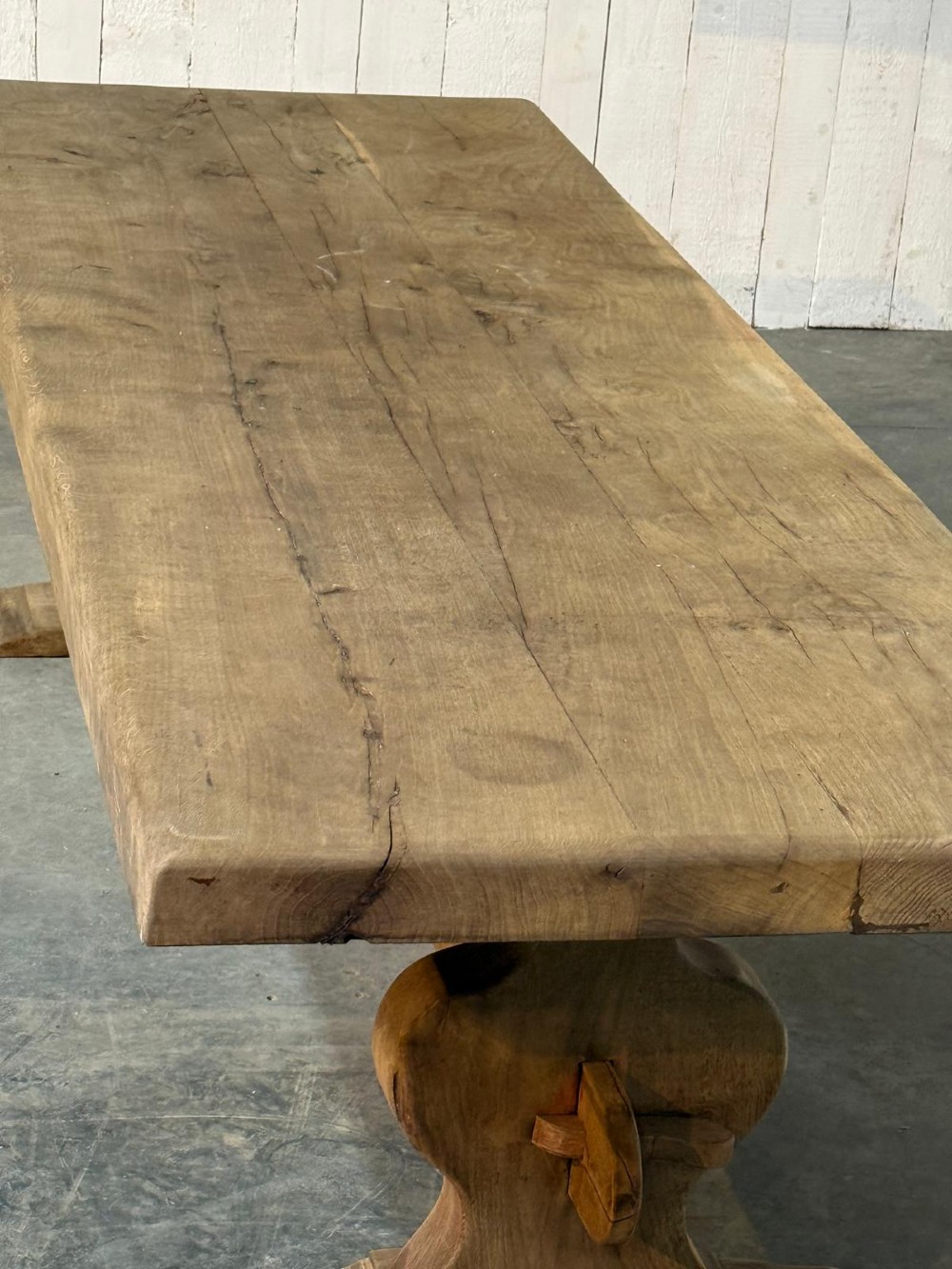 A large rustic French oak dining table featuring a thick timber plank top supported by a sturdy trestle base with a central keyed stretcher. View XIV