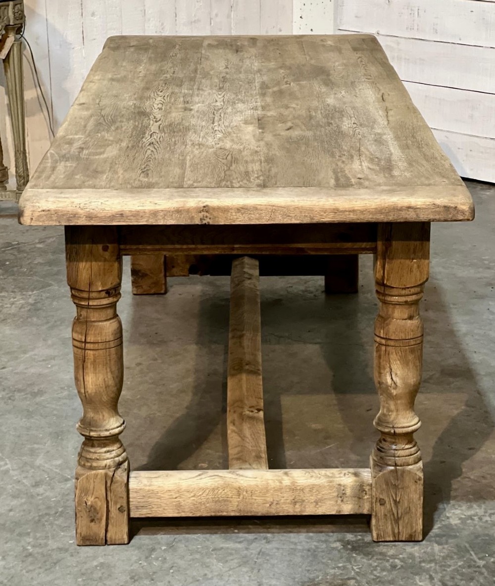 A rectangular bleached oak farmhouse dining table featuring turned legs, a low central stretcher, and a breadboard top. View VII