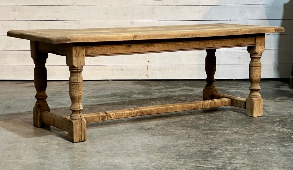 A rectangular bleached oak farmhouse dining table featuring turned legs, a low central stretcher, and a breadboard top. View X