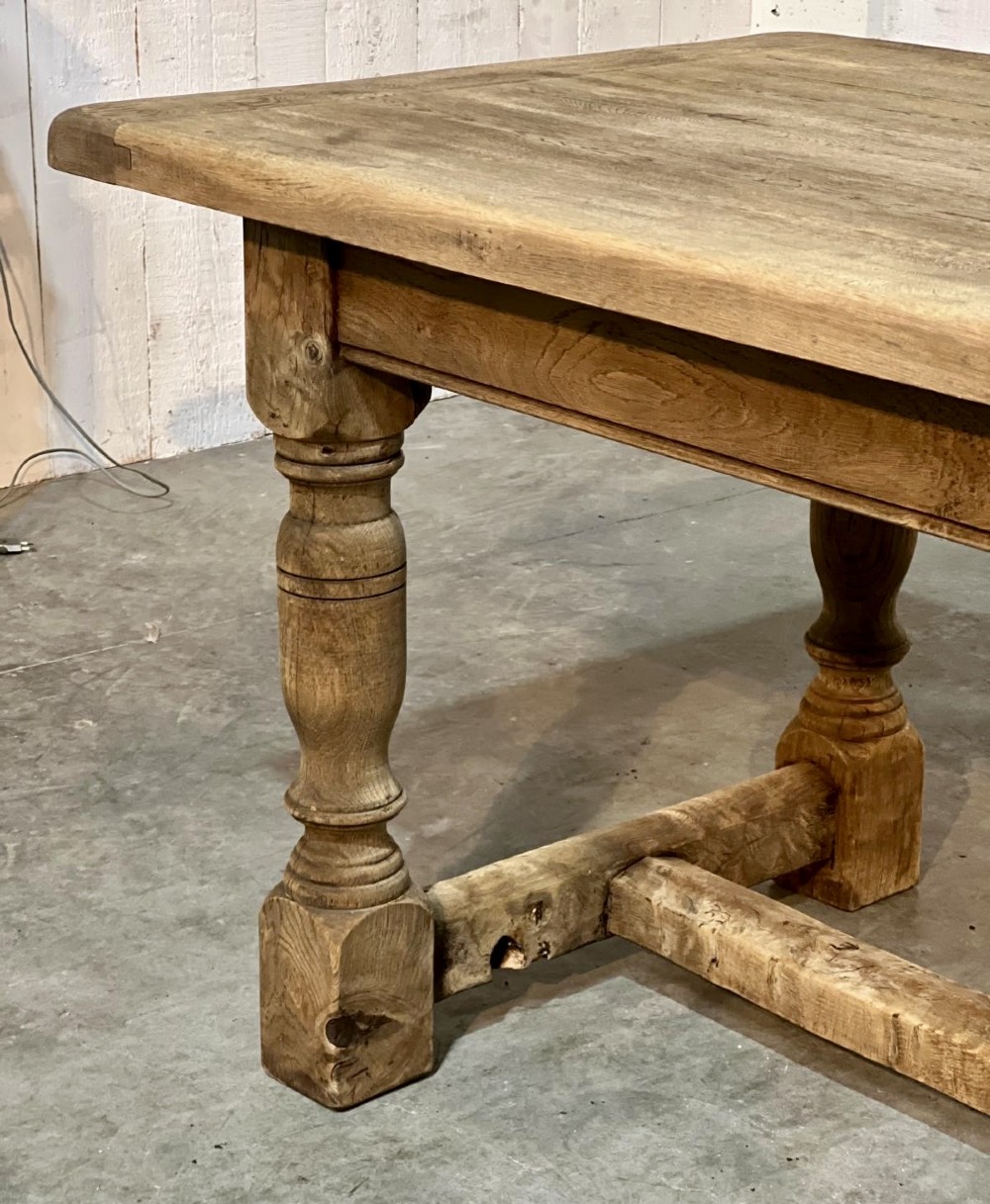 A rectangular bleached oak farmhouse dining table featuring turned legs, a low central stretcher, and a breadboard top. View XIII