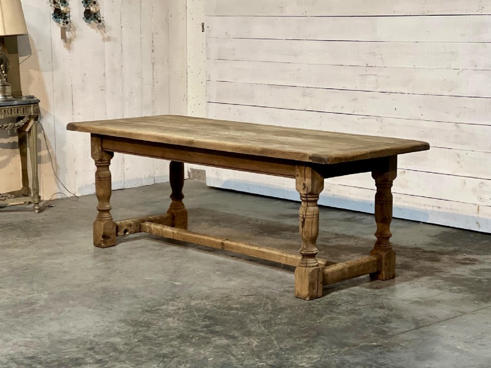 A rectangular bleached oak farmhouse dining table featuring turned legs, a low central stretcher, and a breadboard top. View XV