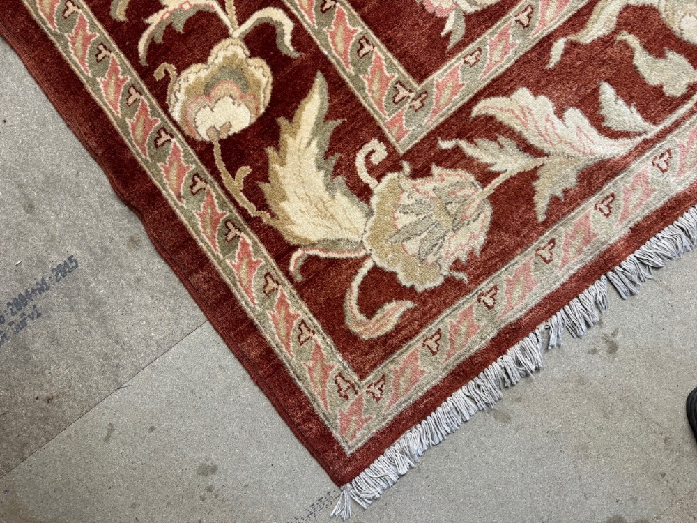 A large woven wool carpet featuring a deep red field decorated with cream and sage green floral scroll motifs and enclosed within a matching multi-tiered border. View II