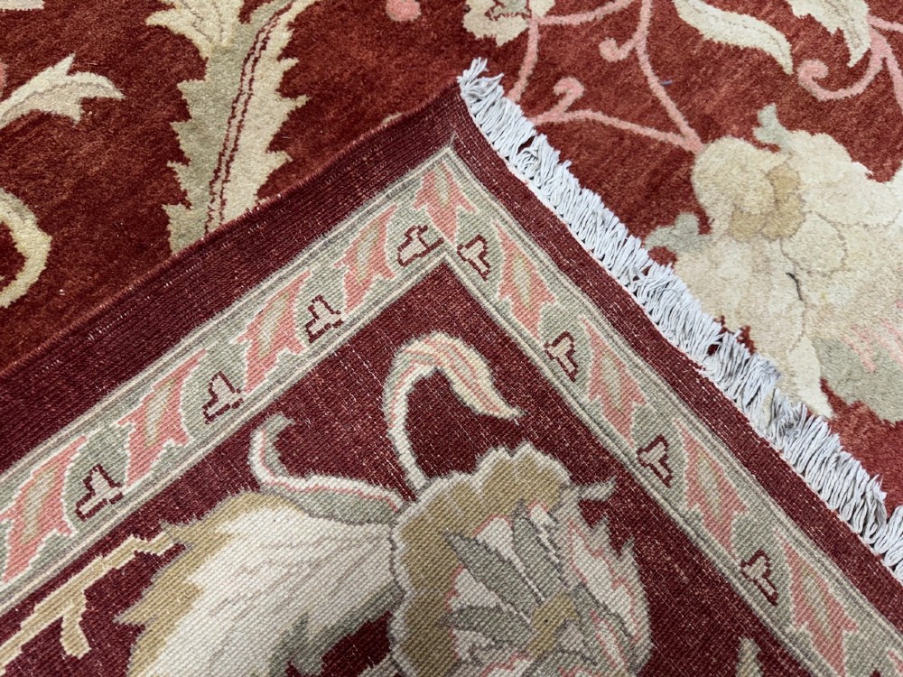 A large woven wool carpet featuring a deep red field decorated with cream and sage green floral scroll motifs and enclosed within a matching multi-tiered border. View IV