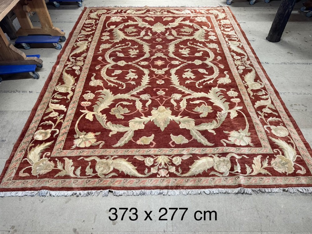 A large woven wool carpet featuring a deep red field decorated with cream and sage green floral scroll motifs and enclosed within a matching multi-tiered border. View X