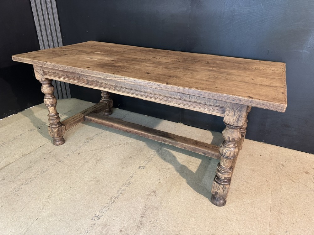 A solid oak farmhouse dining table with a thick plank top, turned baluster legs, and a low central stretcher rail.